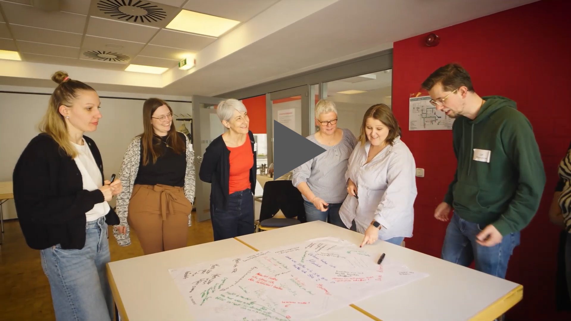 Studierende stehen um einen Tisch, auf dem ein Plakat liegt